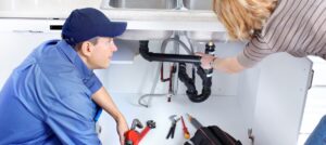 Plumber vs. technician. A plumber looks under the sink to find a leak.